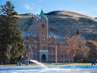 two staff members use a hose to fill the ice rink on the oval