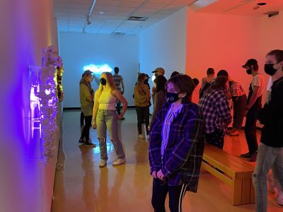 view of the gallery lit with purple, teal, and red neon lights with a light crowd of people in attendance