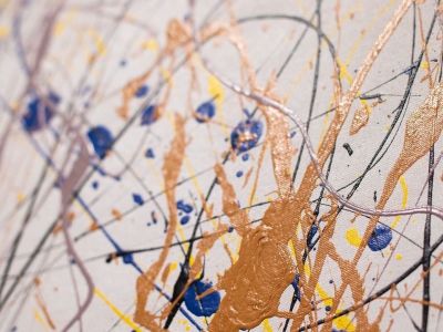 closeup of abstract drip painting in gold and deep blue on white with splashes of yellow and lavender