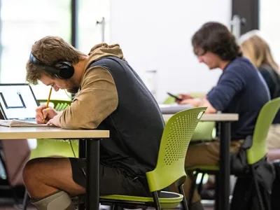 student writes in a notebook while wearing headphones
