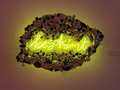 neon art with ceramic frame, neon is yellow and says 'beschamt,' frame is in the shape of a lemon made of ceramic lemons and flowers