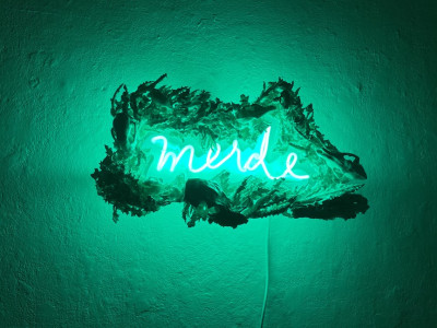 green neon that says merde with ceramic frame made of skulls and thistles