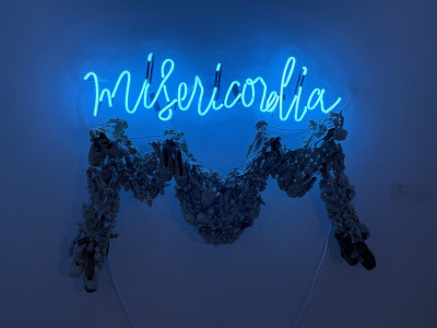 neon sign in cursive 'misericordia' with a ceramic garland below, blue
