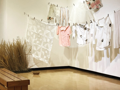 double stranded clothesline with a sheer white quilt, felted pieces, and various items of clothing with poetry text and old-fashioned clothespins. some of the clothing is scorched and burnt