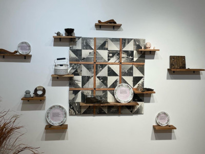 center is a wooden 'quilt' made from cutup old photographs, with shelves on and surrounding it, featuring various found objects, ceramic plates with poems, a jar of dirt, and rusted junk