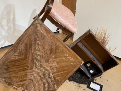 an end table with poem inscribed and a vintage chair with pink cushion hang suspended in the air next to a bookshelf that appears to be sinking into the ground