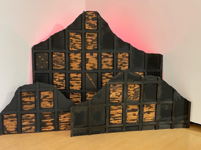 wooden mountain forms with grids, poems are etched into grids much like stained glass windows. three mountains are backlit with red light