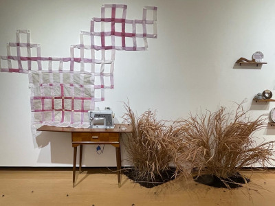 left to right: pink and purple paper quilt in honeycomb shape on wall, vintage sewing machine, dried grasses and dirt