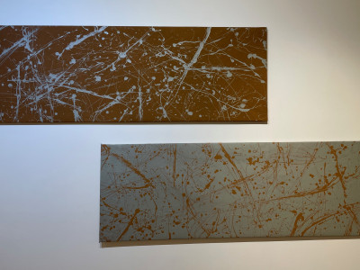 two abstract paintings hanging horizontal, top is brown background with silver paint, bottom is silver with brown paint