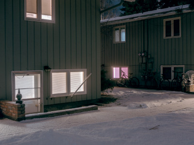 two green paneled apartment buildings in winter, at night, in snow. a basement apartment emits a pink glow