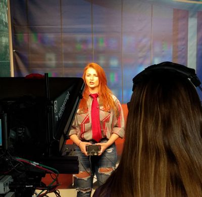 Woman stands in front of camera and teleprompter