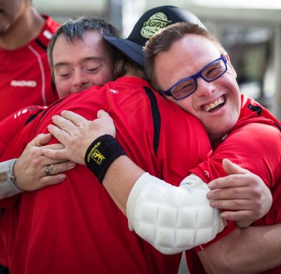 Three young people wearing sports uniforms hug each other while one smiles at the camera