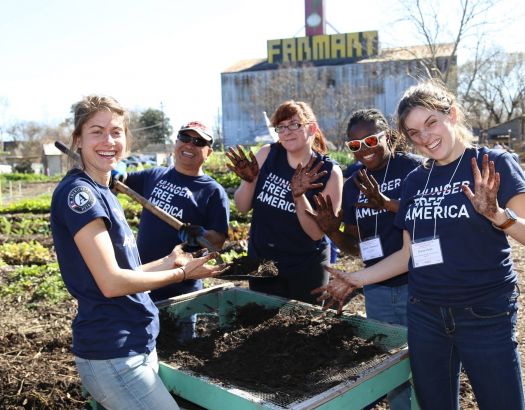 four americorps volunteers stand around a soil sifter in a garden