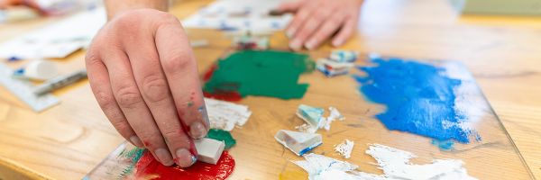 close up view of a hand mixing paint on a piece of glass