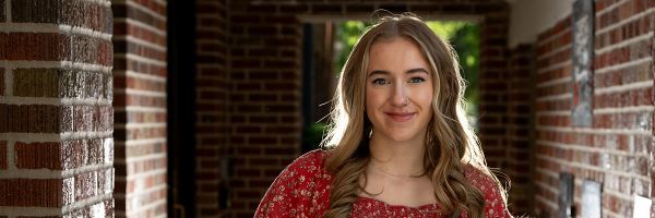student smiling for camera in a brick lined outdoor hallway