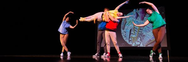 two students holding one up horizontally while two other students bend and point their hands at either side of them