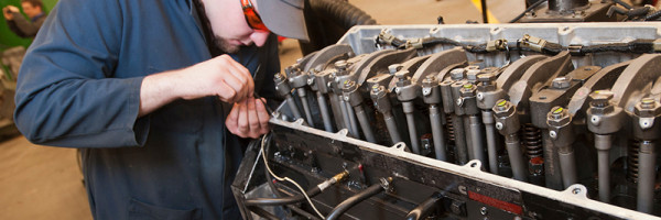 student working closely on a diesel engine