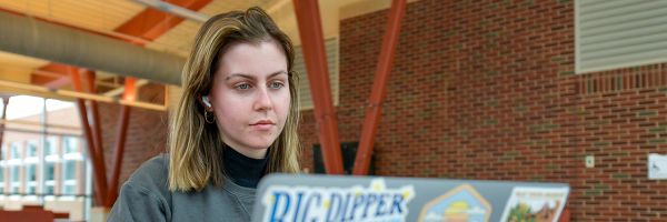 student with headphones in working on their laptop outside