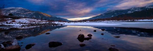 partially frozen lake with mountains in the background under a dramatic sky