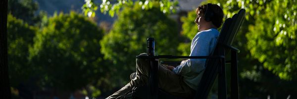 student listening with headphones relaxing in a chair outside on the UM campus