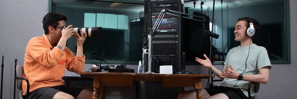 two people in a recording student with the person on the left taking a photograph of the person in headphones on the right