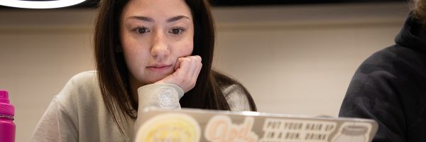 close up view of a student with their hand on their chin while looking at a laptop
