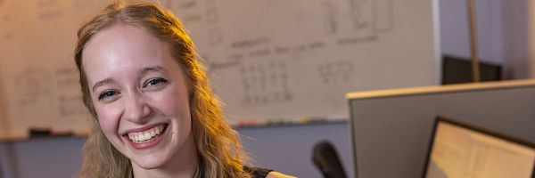smiling student in front of a whiteboard filled with writing and figures