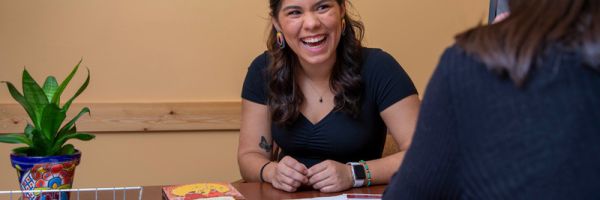 two people working at a table with books and paper while one laughs