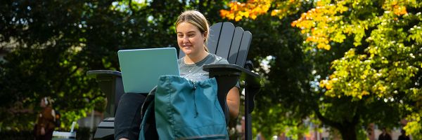 student sitting in a chair outside studying on their laptop