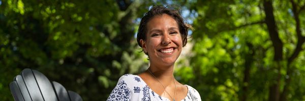smiling person sitting outside with bright green trees in the background
