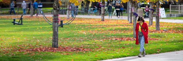 person walking along sidewalk on UM campus with fall landscape behind