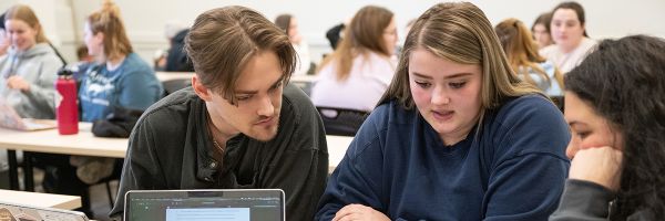 group of students in a classroom working in a group with other groups in the background