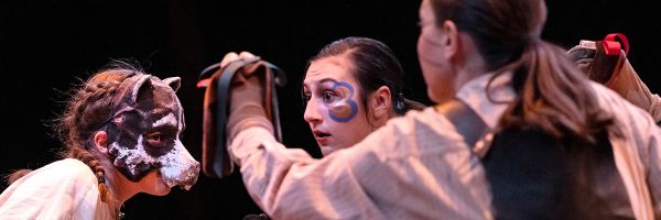 person in animal mask staring at another person in face paint on stage acting