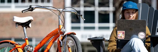 A student studies on a laptop on the Oval at UM with a bike nearby