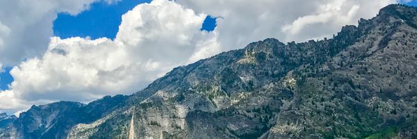rocky, tree covered mountain with cloudy blue sky above