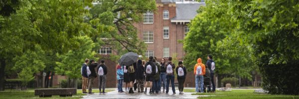 students standing in a group on a walking path at the university in the rain