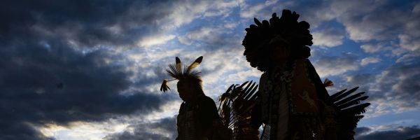 silhouettes of two people in tradition Native American clothing in front of a dramatic sky