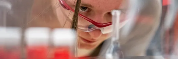 A UM student wearing safety glasses leaning down and looking at beakers in the Chemistry lab at the 51�Թ���.