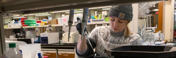 student working with a pipette in a laboratory filled with equipment and storage containers