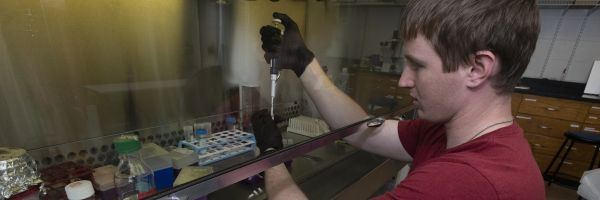 student using a pipette in a laboratory surrounded by other lab equipment