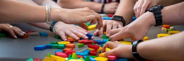 hands of many people reaching into a pile of differently colored and shaped blocks