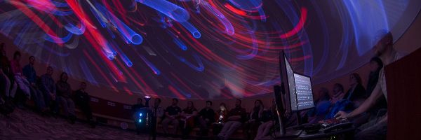 group of students looking at swirling colors and shapes on the ceiling of a planetarium