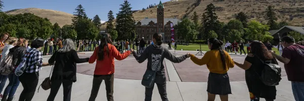 group of students holding hands around the center of the UM oval