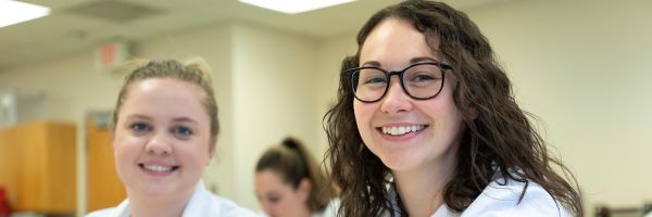 two health students in lab coats posing and smiling