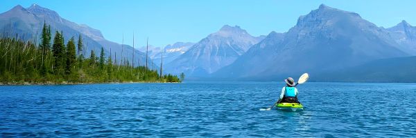 A paddler kayaks across a lake in the mountains