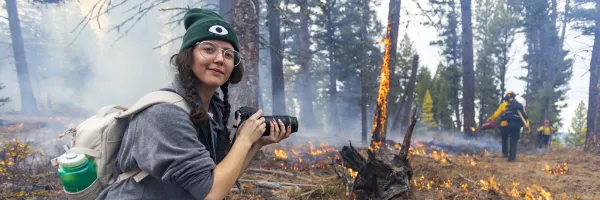 A UM Journalism student kneels with a camera and takes photos of a controlled burn in the University of Montana's Lubrecht Experimental Forest near Missoula, MT.