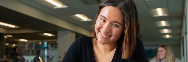 student smiling while studying at a table in the Missoula College library