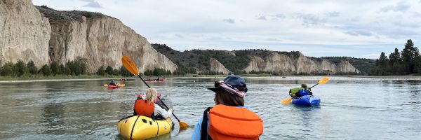 view from the back of a kayak while paddling down a river with a group of other kayakers