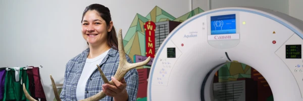 A UM PhD student in the School of Forestry, sitting by a CT Scan machine holds an antler.