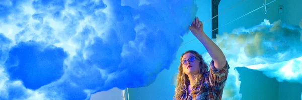 A UM School of Visual and Media Arts student adjusts a hanging cloud piece before an art gallery show.